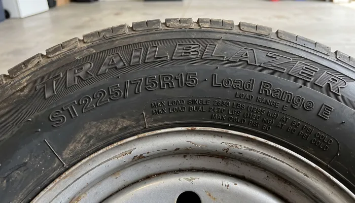 Close-up of a trailer tire sidewall displaying the size ST225/75R15, Load Range E, and a Max Cold PSI of 80. Properly inflating your RV tires to the maximum cold pressure reduces heat-generating sidewall flex, solving one of the main reasons why do trailer tires blow out in the summer.