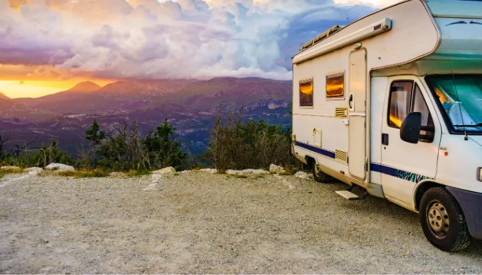 A white RV parked at a scenic mountain overlook during a beautiful summer sunset. To ensure your road trips stay this peaceful, every driver must understand exactly why do trailer tires blow out in the summer and how to prevent heat-related tire failures.