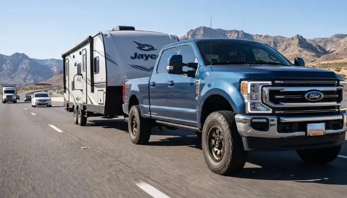 A heavy-duty Ford F-250 truck towing a large trailer on the highway, relying on the best 17" Load Range E tires for maximum payload capacity and towing safety.