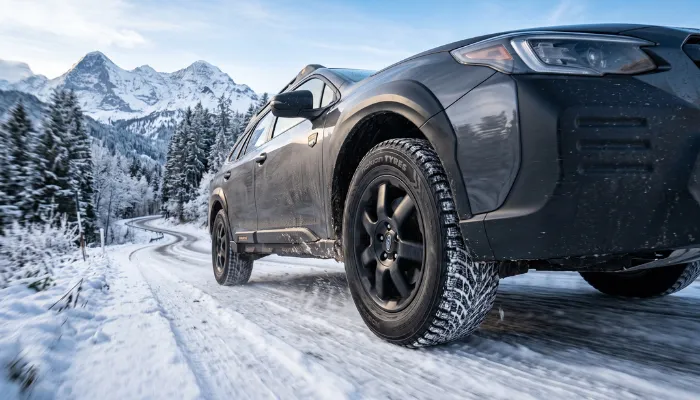 Discontinued Blizzak WS90 winter tire mounted on a car driving safely through packed snow.